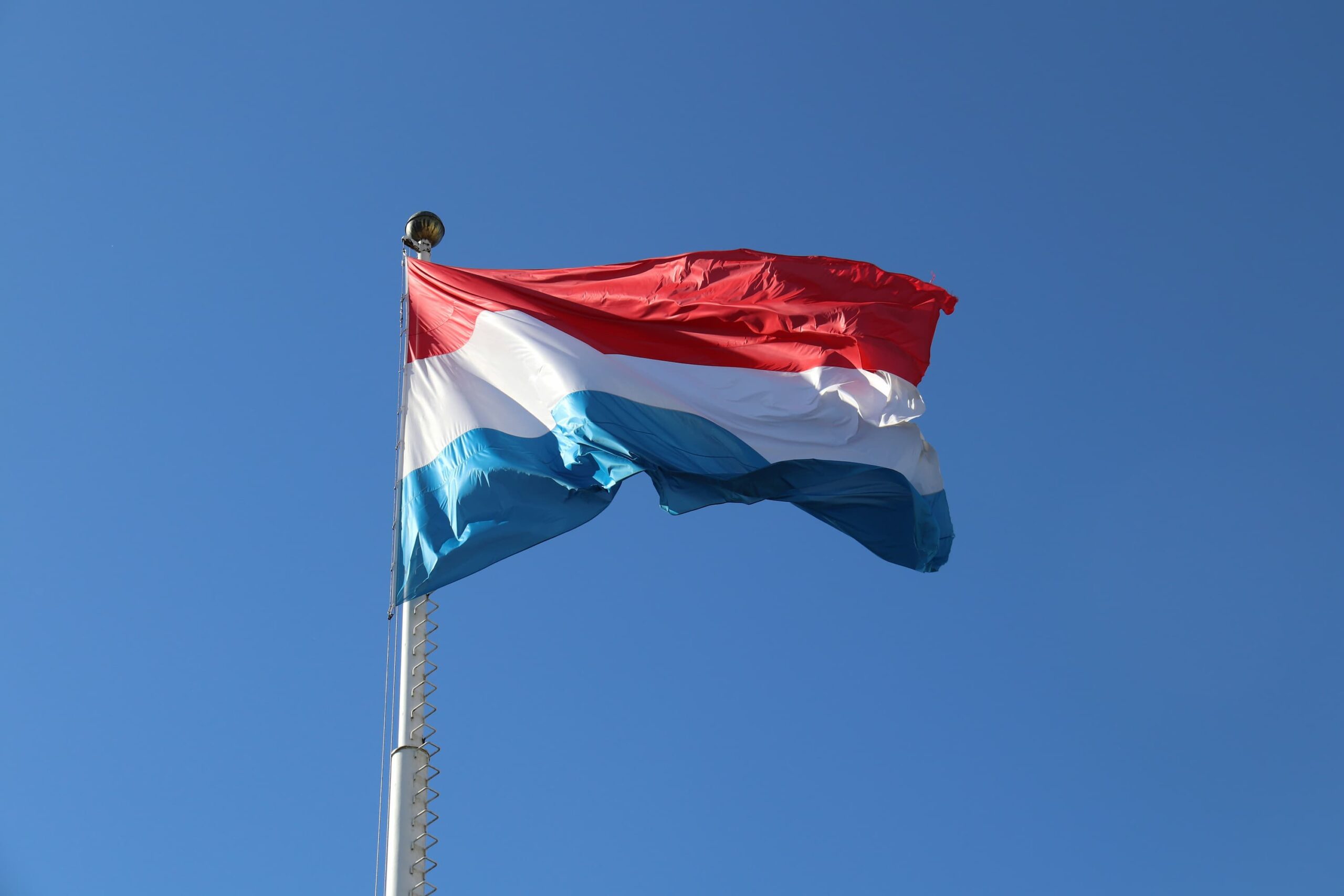 The official flag of Luxembourg flying high on a white flagpole.